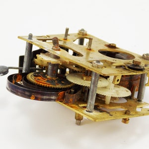 May include: Close-up of a vintage clock mechanism with brass gears and a metal spring. The mechanism is rusty and shows signs of wear and tear.
