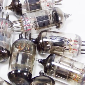 May include: A collection of vintage vacuum tubes with glass casings and metal bases. The tubes have multiple pins and wires inside. Some of the tubes have writing on them.