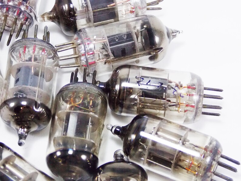 May include: A collection of vintage vacuum tubes with glass casings and metal bases. The tubes have multiple pins and wires inside. Some of the tubes have writing on them.