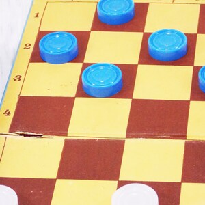 Pode incluir: Um jogo de damas azul e marrom com pe&ccedil;as azuis no tabuleiro. Os n&uacute;meros 1, 2, 3, 4 e 5 s&atilde;o vis&iacute;veis na lateral do tabuleiro.