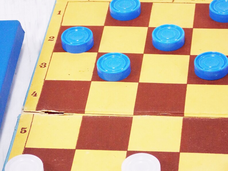 Pode incluir: Um jogo de damas azul e marrom com pe&ccedil;as azuis no tabuleiro. Os n&uacute;meros 1, 2, 3, 4 e 5 s&atilde;o vis&iacute;veis na lateral do tabuleiro.
