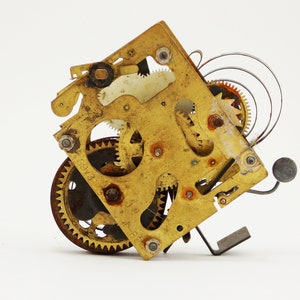 May include: Close-up of a gold-colored clockwork mechanism with intricate gears and a spring. The mechanism is partially disassembled, revealing the inner workings.