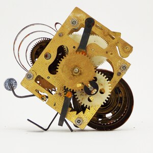 May include: A close-up of a vintage clockwork mechanism with intricate gears and a spring. The mechanism is made of brass and has a worn, aged appearance.