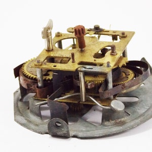 May include: Close-up of a vintage clock mechanism with brass gears, a metal spring, and a rusty metal base.