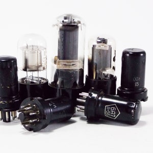 Może przedstawiać: Grupa sześciu zabytkowych lamp elektronowych z czarnymi podstawami i szklanymi wierzchołkami. Lampy są ułożone w grupie na białym tle. Niektóre z lamp mają tekst na boku, w tym "6A1" i "I-56".