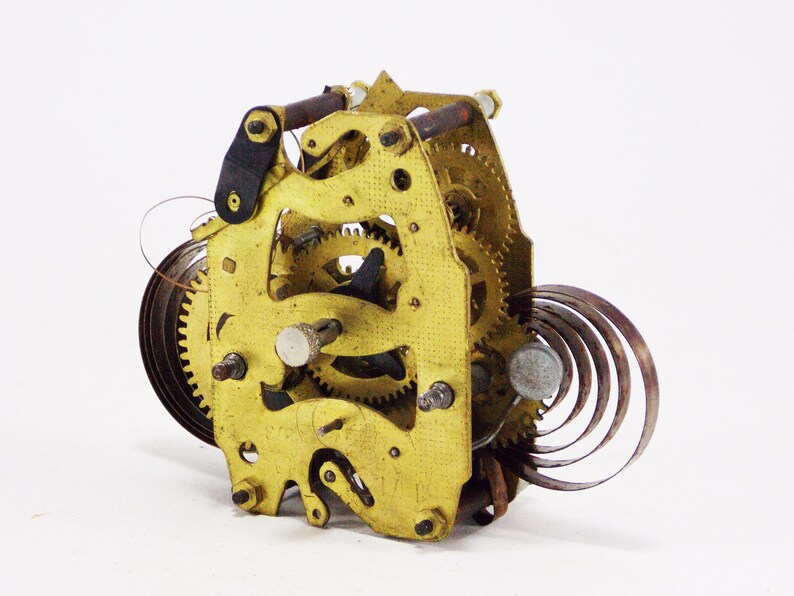 May include: Close-up of a gold-coloured clock mechanism with a spring and gears. The mechanism is made of metal and has a worn, antique look.
