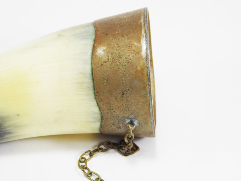 May include: A vintage horn drinking cup with a brass band and chain. The brass band has an inscription that is difficult to read.