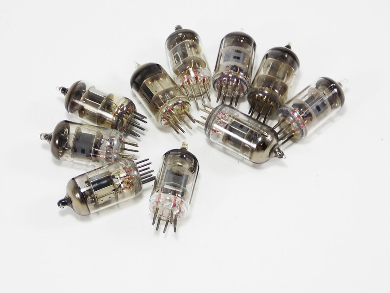 May include: A group of ten vintage vacuum tubes, with a clear glass body and metal base, arranged in a circle on a white surface.