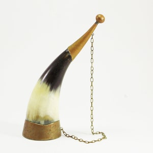 May include: A decorative horn drinking vessel with a brass base and a brass chain attached to the top. The horn is black and white with a natural finish.