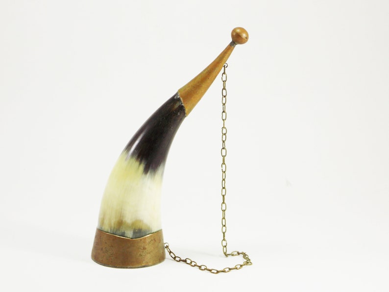 May include: A decorative horn drinking vessel with a brass base and a brass chain attached to the top. The horn is black and white with a natural finish.