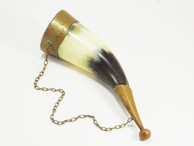 May include: A brown and white horn drinking cup with a brass rim and a brass chain attached to the rim. The chain has a brass ball at the end.