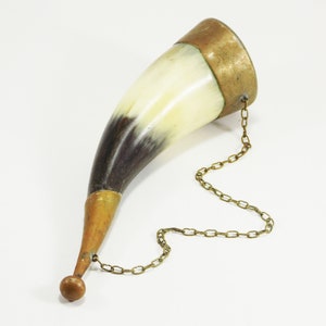 May include: A vintage drinking horn made of horn and brass with a chain attached. The horn is white and brown with a brass tip and a brass band around the top.