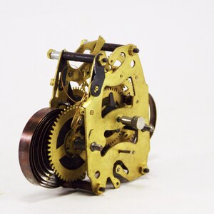 May include: Close-up of a gold-coloured clockwork mechanism with a copper-coloured spring. The mechanism has several gears and a winding key.