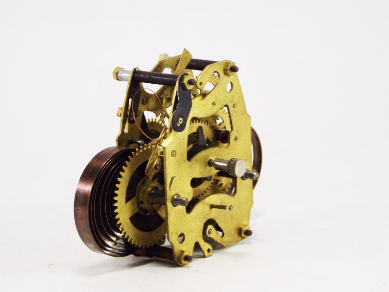 May include: Close-up of a gold-coloured clockwork mechanism with a copper-coloured spring. The mechanism has several gears and a winding key.