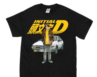 May include: Black t-shirt featuring a yellow and white graphic of a cartoon character standing in front of a white car. The text "INITIAL D" is written in yellow above the graphic.