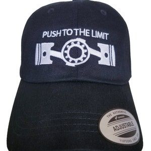 May include: Black baseball cap with white embroidery that reads "PUSH TO THE LIMIT" and a stylized image of a crankshaft. The cap has an adjustable strap with a gray label that reads "THE AUTHENTIC YUPOONG ADJUSTABLE YUPOONG SINCE 1974."