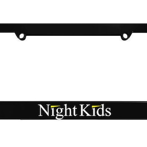 May include: A rectangular black license plate frame featuring the text Night Kids in white lettering with a small yellow accent line above the letter i. The frame includes two circular mounting holes at the top for vehicle attachment.