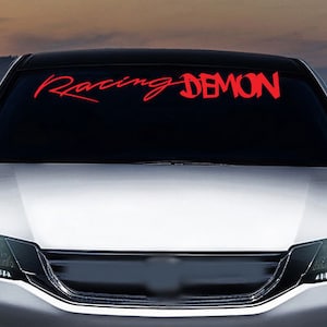 Könnte beinhalten: Ein weißes Auto mit den Worten "Racing Demon" in roten Buchstaben auf der Windschutzscheibe.
