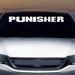 May include: A white car with a windshield decal that reads "PUNISHER" in a bold, white font. The car is parked in front of a body of water with a mountain range in the background.