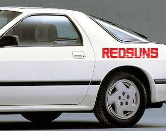 May include: A white car with a red "REDSUNS" decal on the side. The car is a coupe with a black stripe along the bottom of the doors.