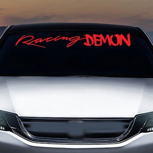 Könnte beinhalten: Ein weißes Auto mit den Worten "Racing Demon" in roten Buchstaben auf der Windschutzscheibe.