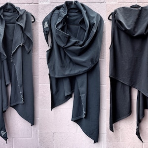 May include: A black hooded vest with a long, asymmetrical hemline. The vest is made of a soft, drapey fabric and has a relaxed fit. The hood is large and can be worn up or down.