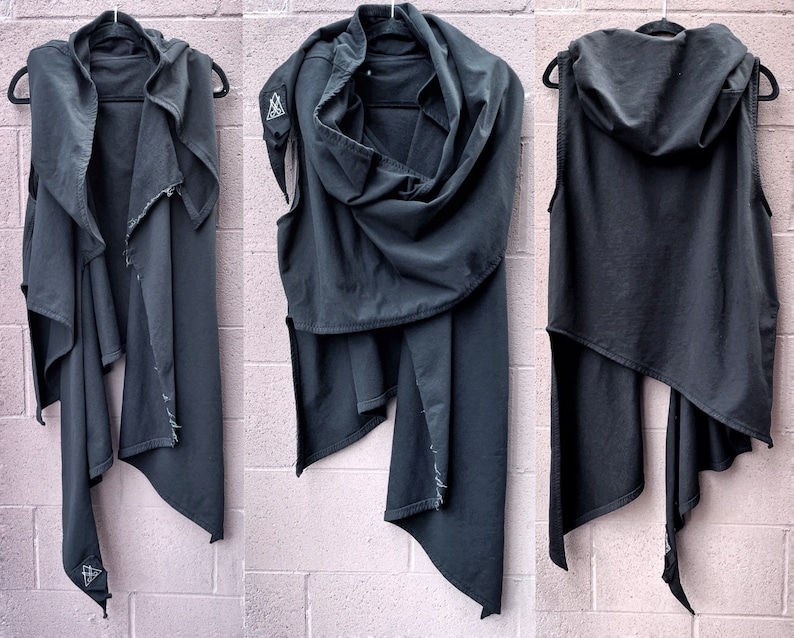 May include: A black hooded vest with a long, asymmetrical hemline. The vest is made of a soft, drapey fabric and has a relaxed fit. The hood is large and can be worn up or down.