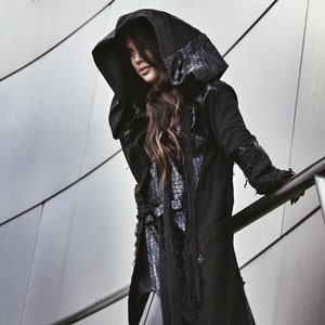 May include: A black hooded jacket with a long, flowing design and a textured pattern on the hood. The jacket has a frayed hem and sleeves, giving it a distressed look.