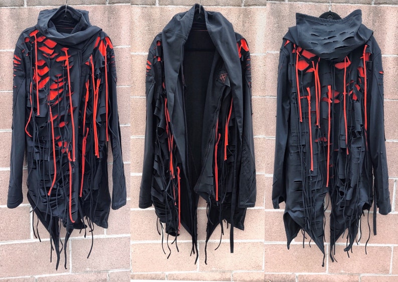 May include: Black hooded jacket with red accents and distressed detailing. The jacket has long sleeves and a long, asymmetrical hemline. The fabric is frayed and has a ripped look.