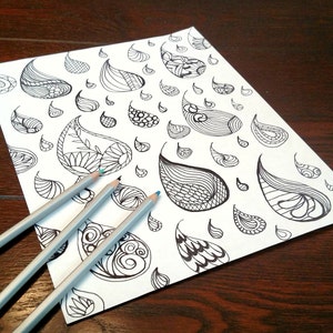 May include: A white sheet of paper featuring a black paisley pattern, accompanied by three grey pencils with blue tips. The paisley designs vary in size and shape, each with detailed internal patterns.
