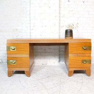 May include: A wooden desk with two drawers on each side. The desk has brass hardware and a light wood finish.