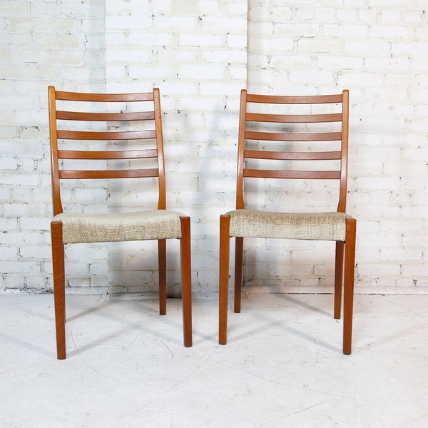 May include: Two wooden chairs with a light brown finish and beige fabric seats. The chairs have a ladder back design with horizontal slats.