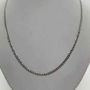 May include: A silver curb chain necklace on a white display stand.