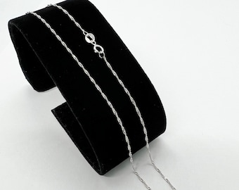 May include: A silver chain necklace with a delicate, twisted design. The chain is displayed on a black velvet background.