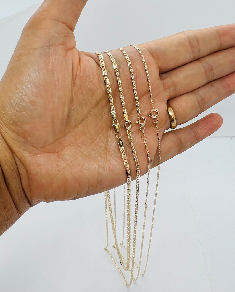 May include: Four gold-coloured necklaces with various chain styles are shown. The chains include a mariner link, a rope chain, and a box chain. Each necklace has a clasp. The necklaces are presented against a light background.