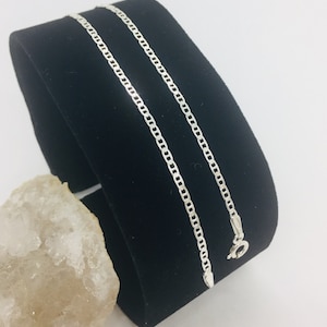 May include: A silver chain necklace with a lobster clasp. The chain is on a black velvet display stand.