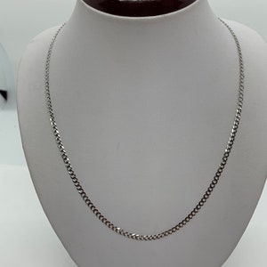 May include: A silver curb chain necklace on a white display stand.