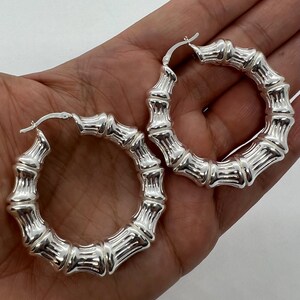 May include: A pair of silver-colored bamboo hoop earrings. The earrings have a textured, segmented design, resembling bamboo stalks. The hoops are shown against a neutral background.