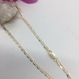 May include: A gold chain necklace with a delicate, textured design. The chain is made of a thin, flat link with a subtle, diamond-cut pattern.