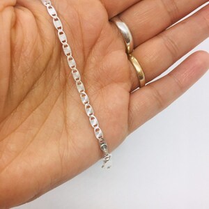 May include: A silver chain bracelet with a delicate, patterned design. The chain is made of small, oval-shaped links.