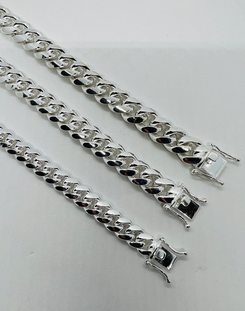 May include: Three silver curb chain necklaces of varying lengths. The chains are made of thick, interlocking links.