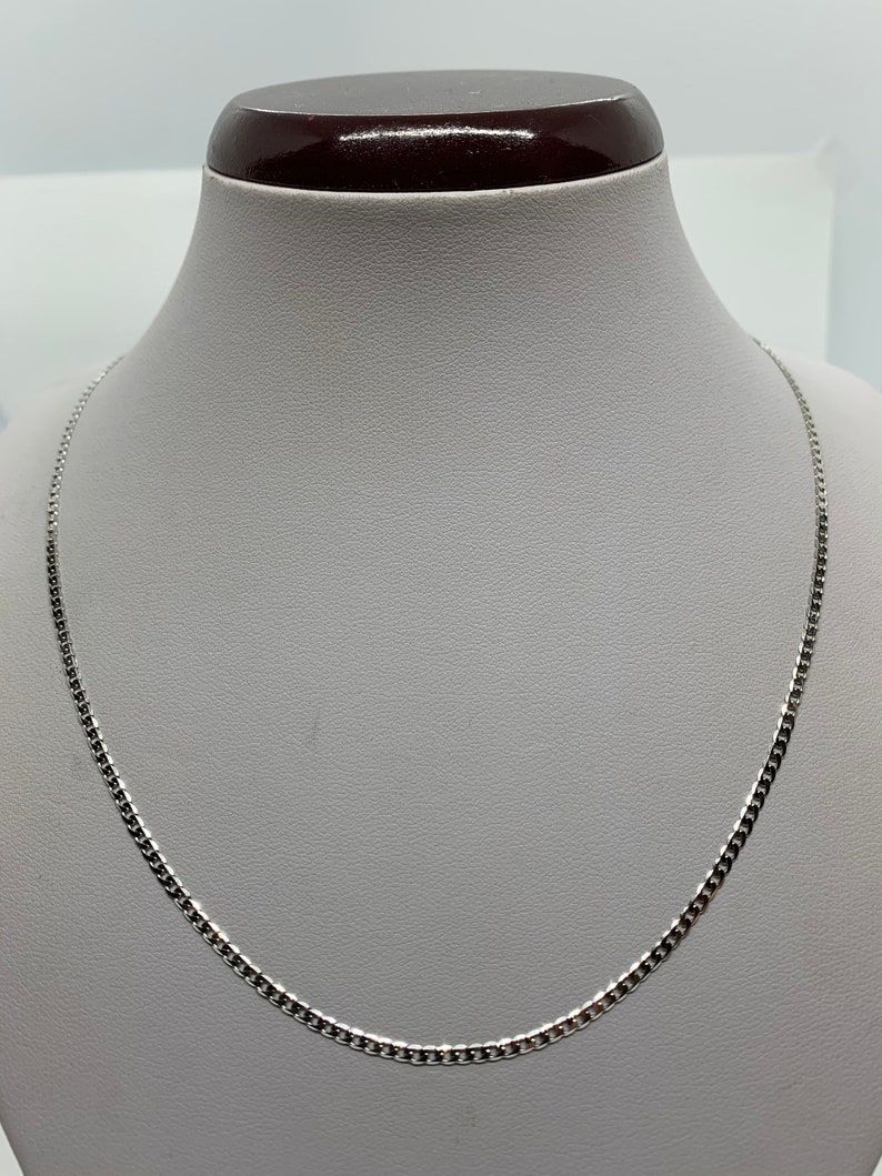 May include: A silver chain necklace on a white mannequin bust.