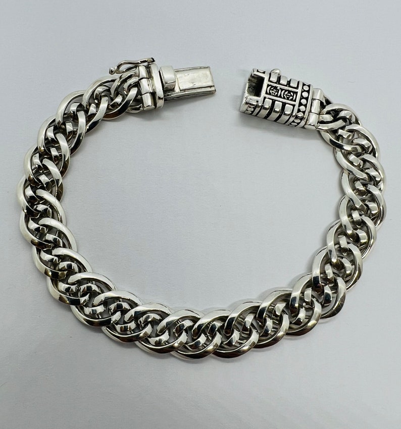 Op de afbeelding: Een zilveren kettingarmband met een gedetailleerde sluiting. De ketting is gemaakt van meerdere verweven schakels.