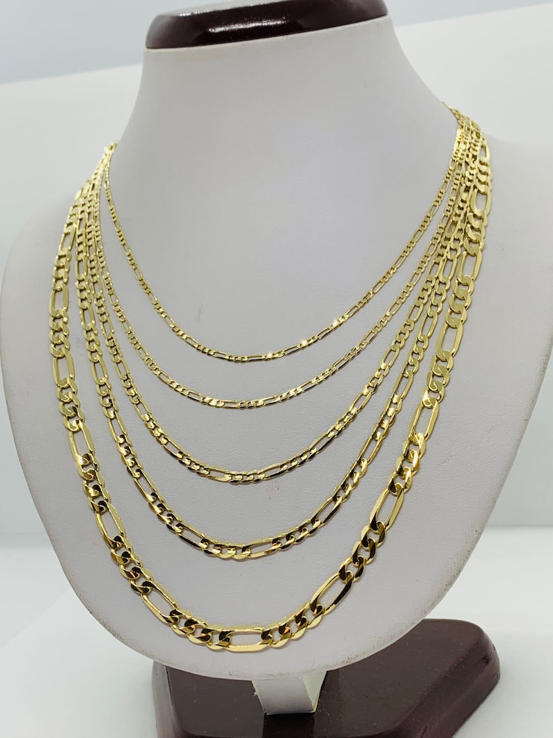 May include: A set of six gold chain necklaces of varying widths, displayed on a white mannequin bust.