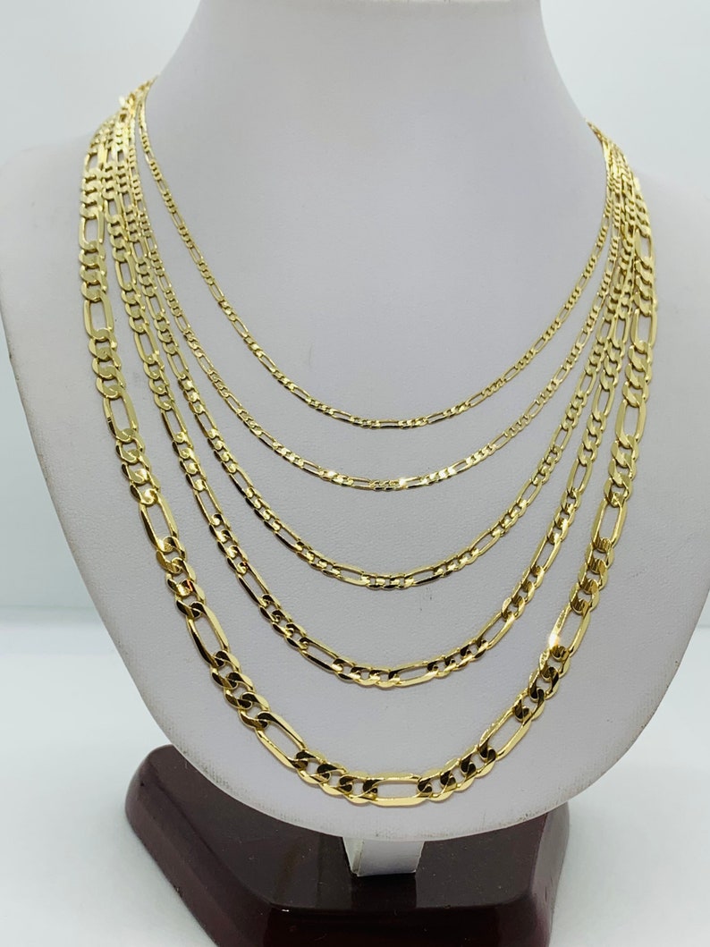 May include: A set of six gold chain necklaces of varying widths, displayed on a white mannequin bust. The chains are all made of a classic, flat, oval-shaped link.