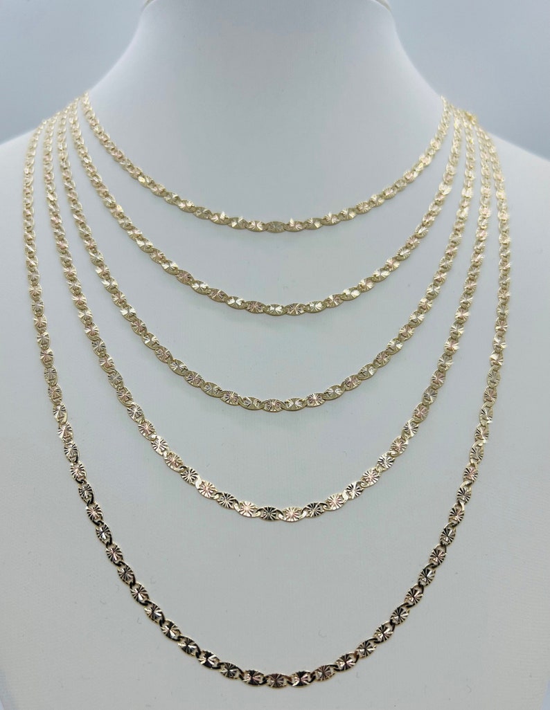 May include: A set of six gold chains with a diamond-cut design. The chains are layered on a white mannequin bust.