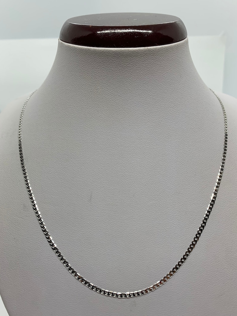 May include: A silver chain necklace with a curb link style. The chain is on a white mannequin bust.