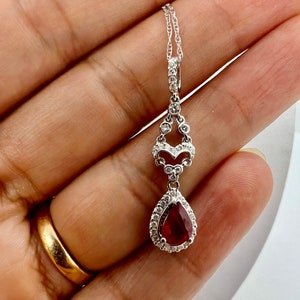 May include: A silver necklace with a pear-shaped red gemstone pendant surrounded by smaller clear gemstones. The pendant is attached to a delicate silver chain.
