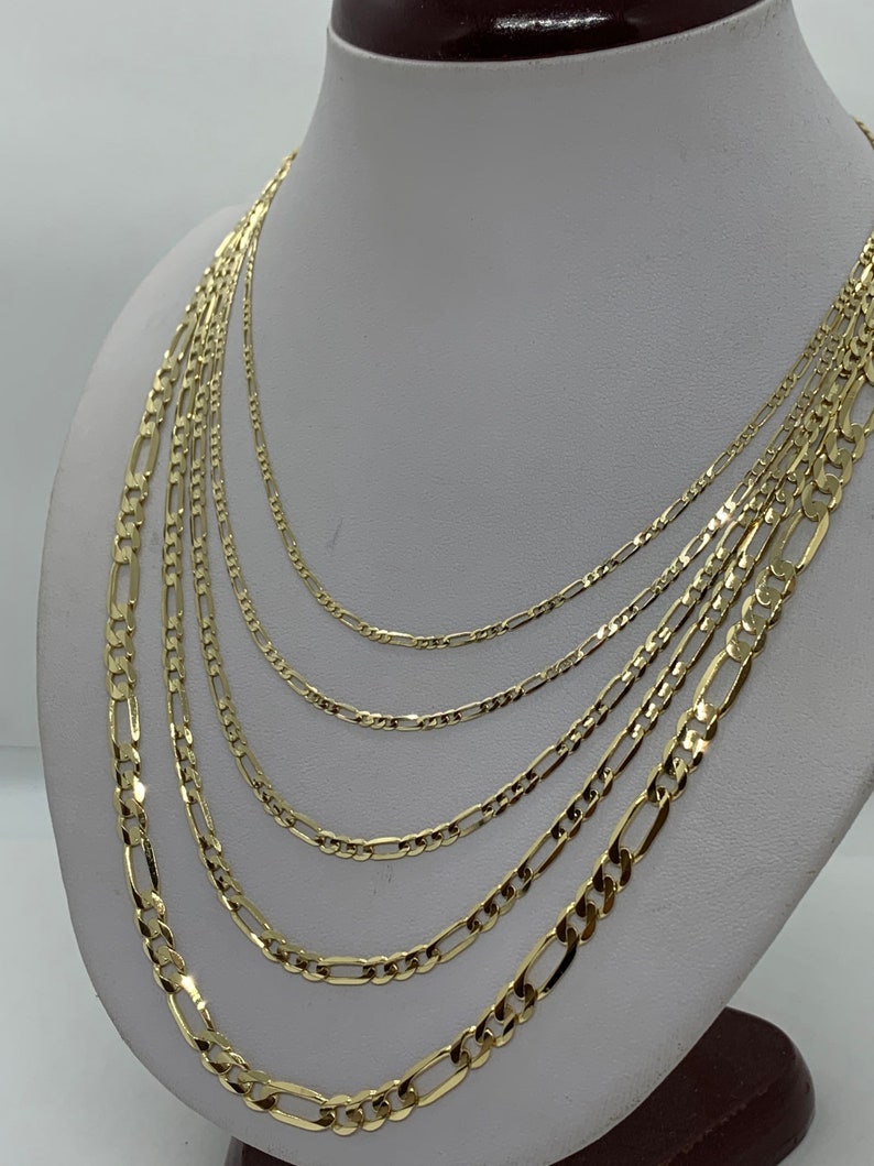May include: A set of six gold chain necklaces of varying widths, displayed on a white mannequin bust. The chains are all made of a classic figaro design.