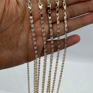 May include: Five gold chains with a diamond-cut design. The chains are arranged in a row, with the shortest chain at the top and the longest chain at the bottom.